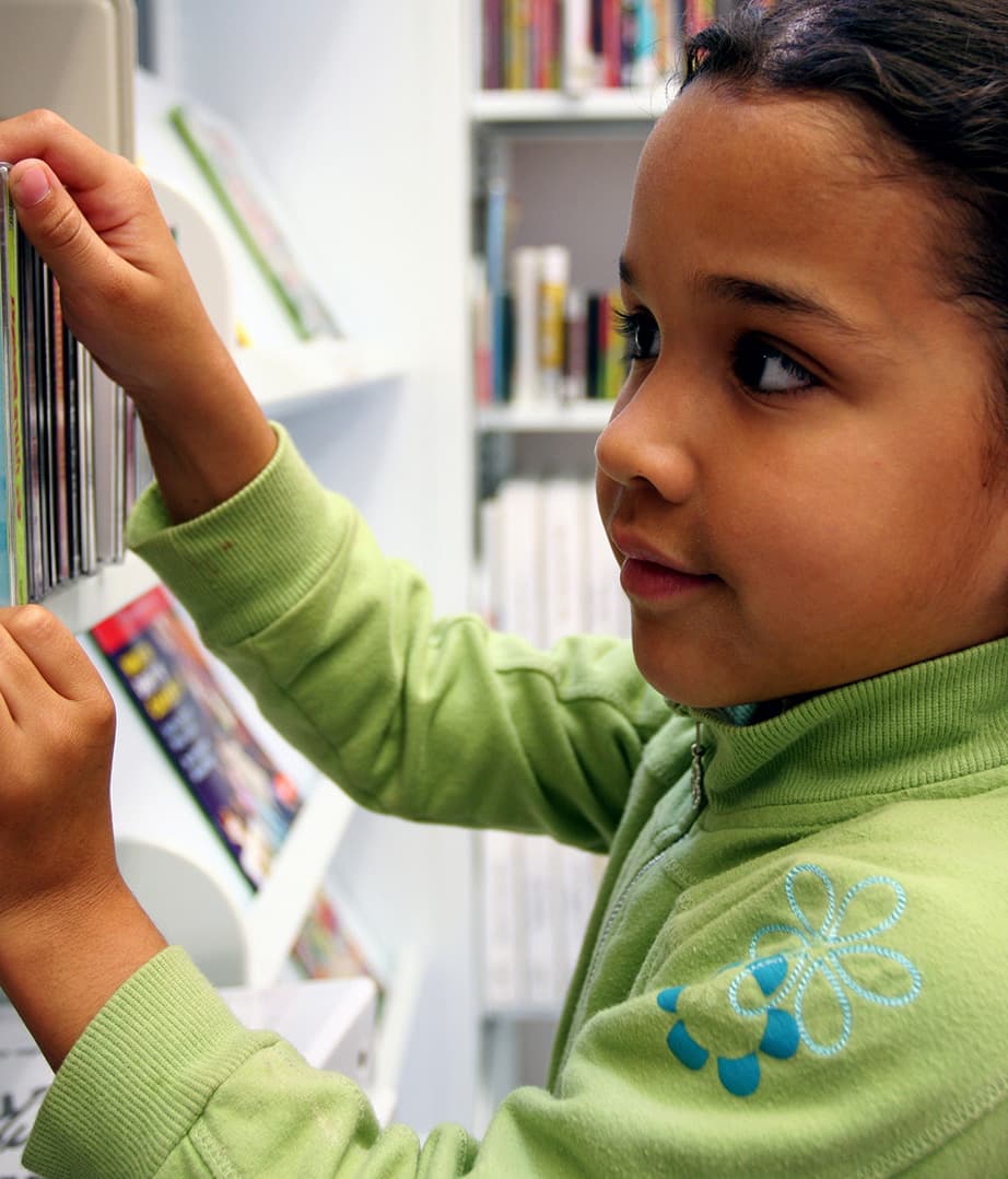 Photo of a young girl looking at books on a library shelf.